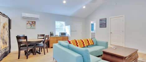 A modern living room with a sofa, dining table, chairs, and a coffee machine.