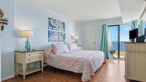 A bedroom with a bed, bedside tables, a dresser, and a view of the sea through a sliding door. - Oceanfront Oasis - Steps to Beach - Pool, Hot Tub & Elevator (Murrells Inlet)