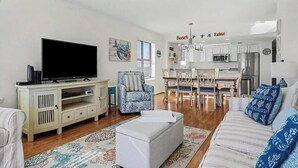 A living room with a flat-screen TV, a sofa, a patterned rug, and a dining area with a table and chairs. - Oceanfront Oasis - Steps to Beach - Pool, Hot Tub & Elevator (Murrells Inlet)