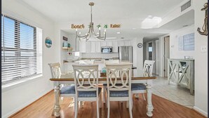 A dining area with a chandelier, white cabinets, and a kitchen in the background. - Oceanfront Oasis - Steps to Beach - Pool, Hot Tub & Elevator (Murrells Inlet)