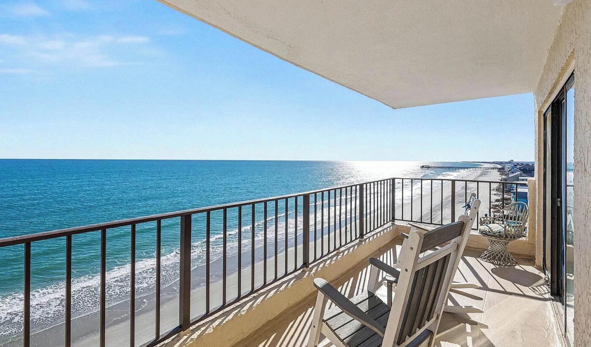 A balcony with a view of the ocean and beach, featuring a railing and a chair.