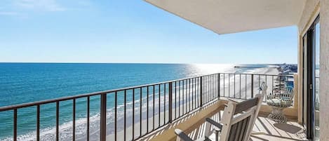 A balcony with a view of the ocean and beach, featuring a railing and a chair.