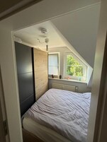 A bedroom with a sloped ceiling, a bed, a window, and a radiator.
