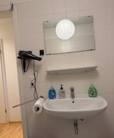 A bathroom with a white sink, a mirror, a hairdryer, and two bottles of liquid soap.