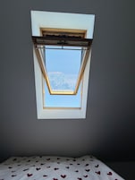 A room with a skylight window, a bed with a heart-patterned bedspread, and a view of a body of water.