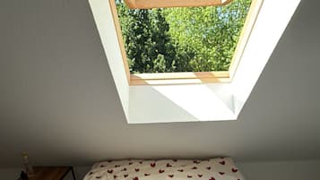 A bedroom with a skylight, a bed with a heart-patterned bedspread, and a small wooden table.
