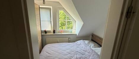Un dormitorio con techo inclinado, cama, ventana y radiador.