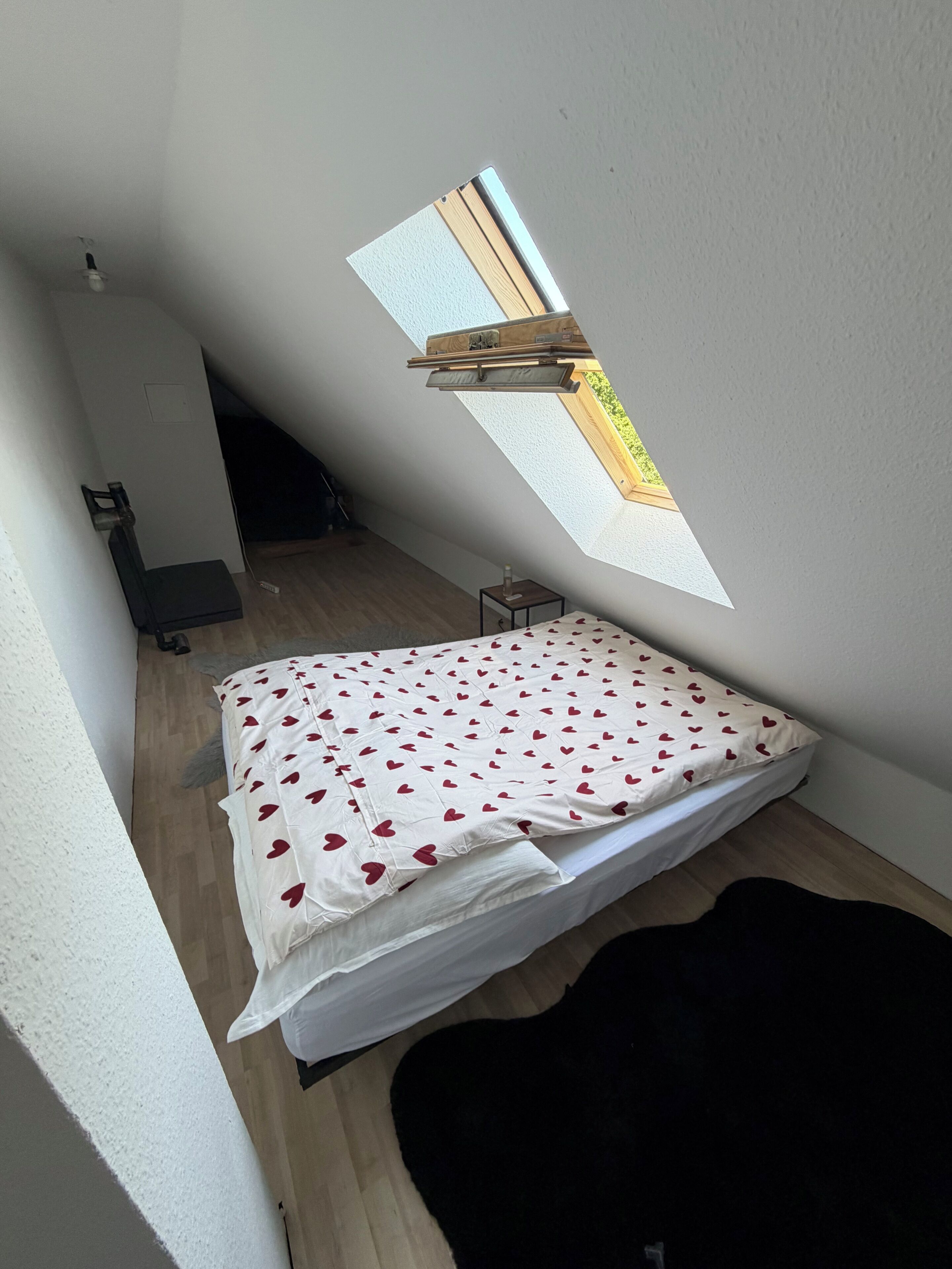 Een kleine kamer met schuine wanden, een bed, dakraam en een houten vloer.