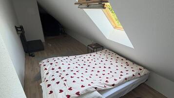 Een kleine kamer met schuine wanden, een bed, dakraam en een houten vloer.