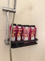 Zona de ducha con grifo cromado y ducha de mano, y un estante con cuatro botellas rosas de champú con la etiqueta 'Schwarzkopf GLISS'.