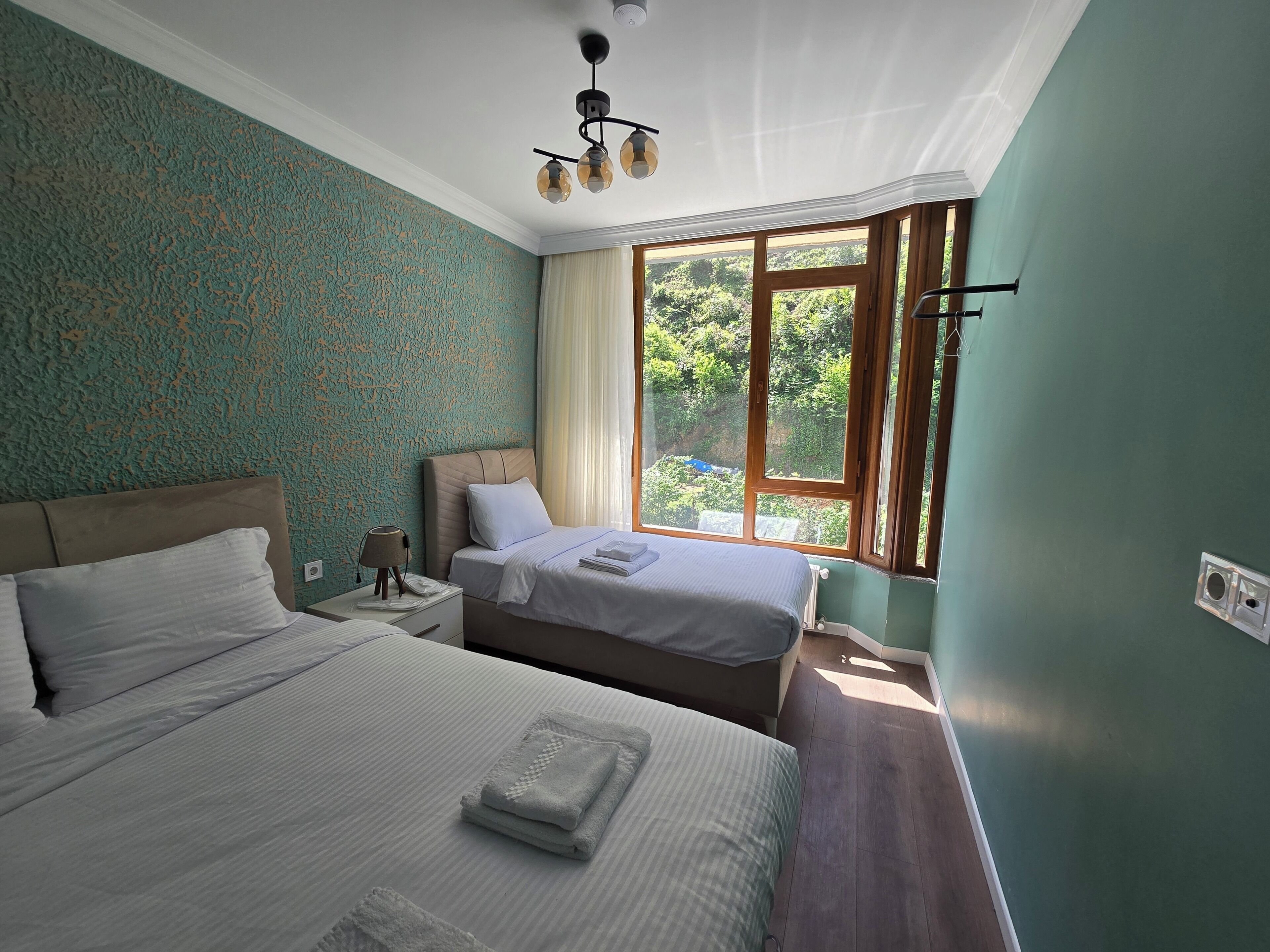 Habitación de hotel con dos camas, una mesita de noche, una lámpara y un ventanal con vistas a zonas verdes.