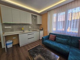 Una cocina moderna con armarios blancos, una estufa integrada y un lavamanos. Hay un sofá azul con un cojín y una mesa de centro de mármol negro.