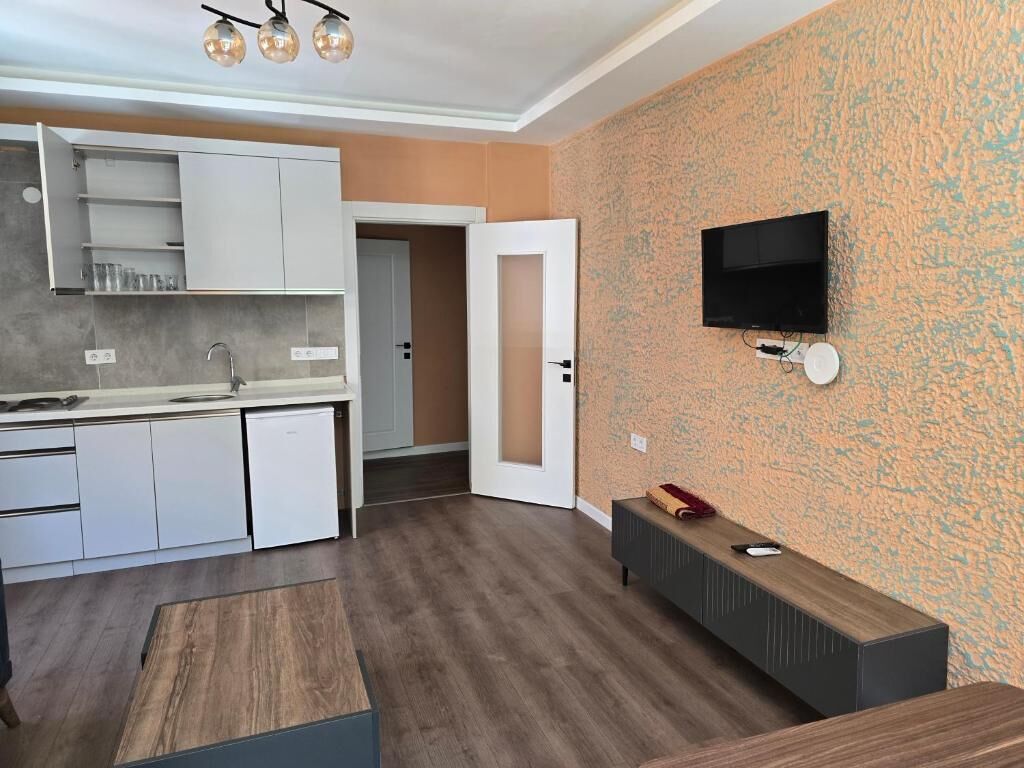 A modern kitchen with white cabinets and a built-in microwave, a wooden dining table, and a television mounted on the wall.