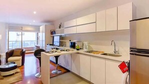 Een moderne keuken met witte kastjes, een eethoek met een tafel en stoelen, en een groot raam.