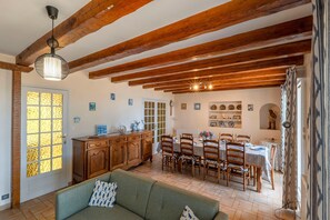 A dining area with wooden beams, a chandelier, and a dining table set for four. - Maison de la Falaise - Accès direct à la plage (Pénestin)