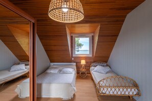 A room with wooden sloped ceilings, a small window with a view, two beds with white bedding, and a woven light fixture. - Maison de la Falaise - Accès direct à la plage (Pénestin)