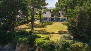 Uma casa com um gramado bem cuidado, uma escadaria visível que leva a um penhasco e uma vista ampla do verde ao redor.