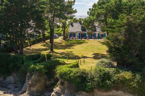 A house with a well-maintained lawn, a visible staircase leading to a cliff, and a clear view of the surrounding greenery. - Maison de la Falaise - Accès direct à la plage (Pénestin)