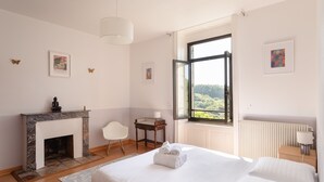 A bedroom with a fireplace, a bed, a chair, a table, and a window with a view. - La chevreuse - Vue mer à moins de 300m de la plage (Lamballe)