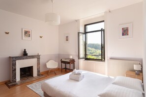 A bedroom with a fireplace, a bed, a chair, a table, and a window with a view. - La chevreuse - Vue mer à moins de 300m de la plage (Lamballe)
