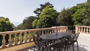 A round metal table with chairs on a balcony with a balustrade, overlooking a mountainous landscape. - La chevreuse - Vue mer à moins de 300m de la plage (Lamballe)
