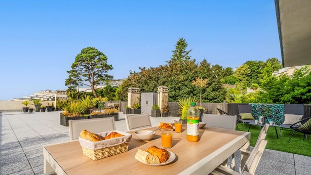 An outdoor dining area with a table set for breakfast, including bread, a bowl, and a glass of orange juice. - La Terrasse de la Rade - Terrasse avec vue mer (Brest)