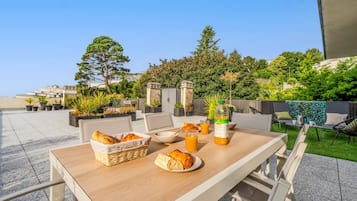Een buitenontbijtplaats met een gedekte tafel, inclusief brood, een kom en een glas sinaasappelsap.