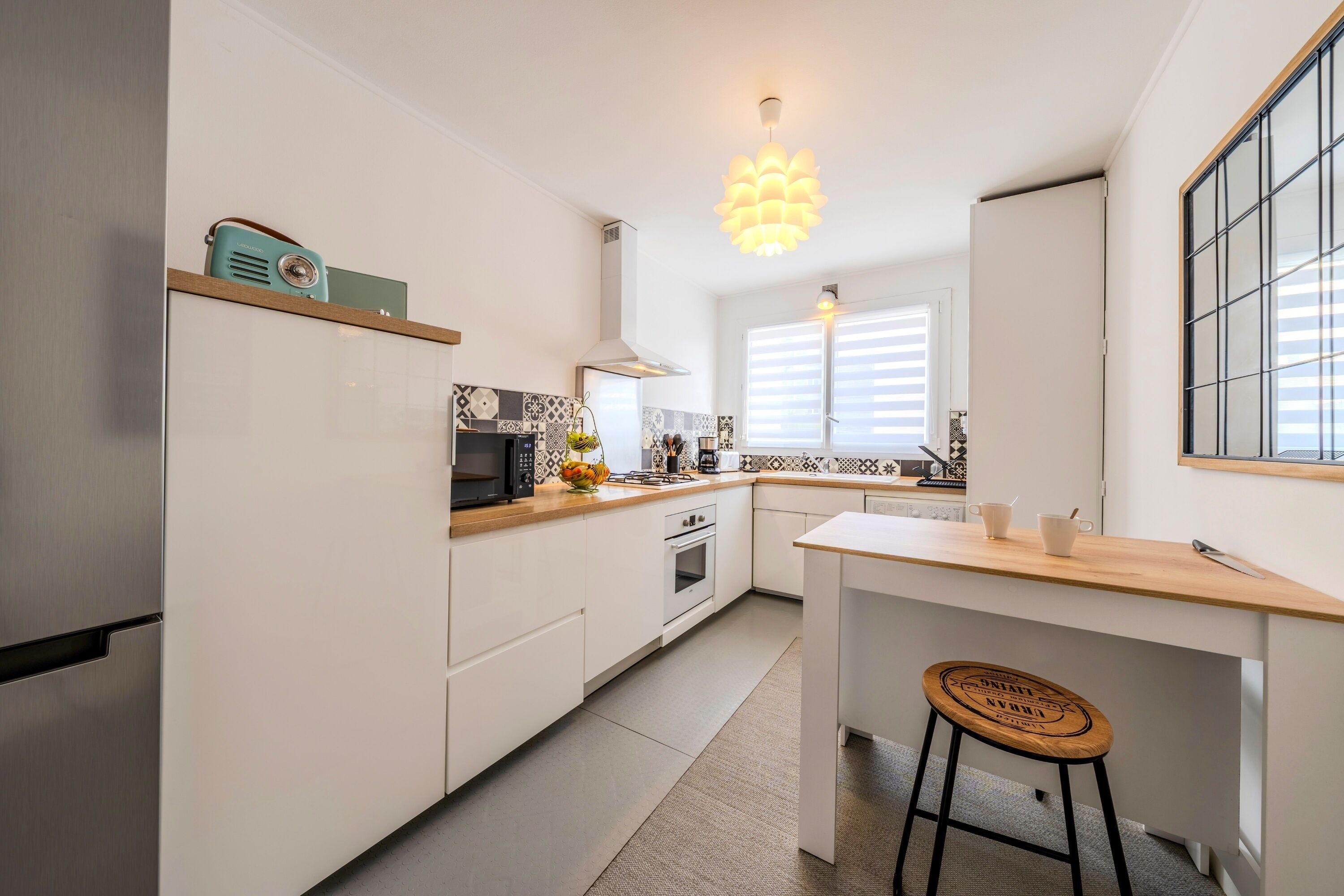 A modern kitchen with white cabinets, a wooden countertop, a built-in oven, a microwave, and a hanging light fixture.