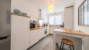 A modern kitchen with white cabinets, a wooden countertop, a built-in oven, a microwave, and a hanging light fixture. - La Terrasse de la Rade - Terrasse avec vue mer (Brest)