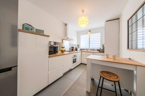 Eine moderne Küche mit weißen Schränken, einer Holzarbeitsplatte, einem eingebauten Backofen, einer Mikrowelle und einer Pendelleuchte.