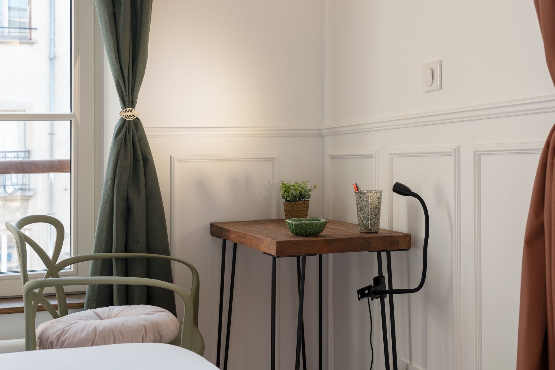 Ein Zimmer mit einem Bett, einem Sessel, einem kleinen Tisch mit Pflanze, einer Dekovase und einer Lampe.
