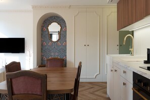 Ein Essbereich mit Holztisch und Stühlen, einem an der Wand montierten Fernseher und einer Küche mit Spüle und Schränken.