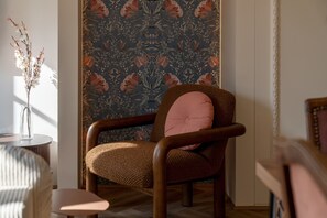 Ein Zimmer mit strukturiertem Wandpapier, einem Holzstuhl mit Kissen, einem kleinen Tisch mit einer Vase und einem Holzboden.