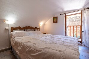 Une chambre à coucher avec une tête de lit en bois, un grand lit, une table de chevet, une lampe fixée au mur, un tableau et un balcon avec vue.