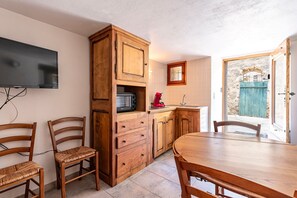 Une cuisine avec des meubles de rangement en bois, un four à micro-ondes et une machine à café rouge. On y trouve une table à manger avec des chaises, ainsi qu’un téléviseur fixé au mur.