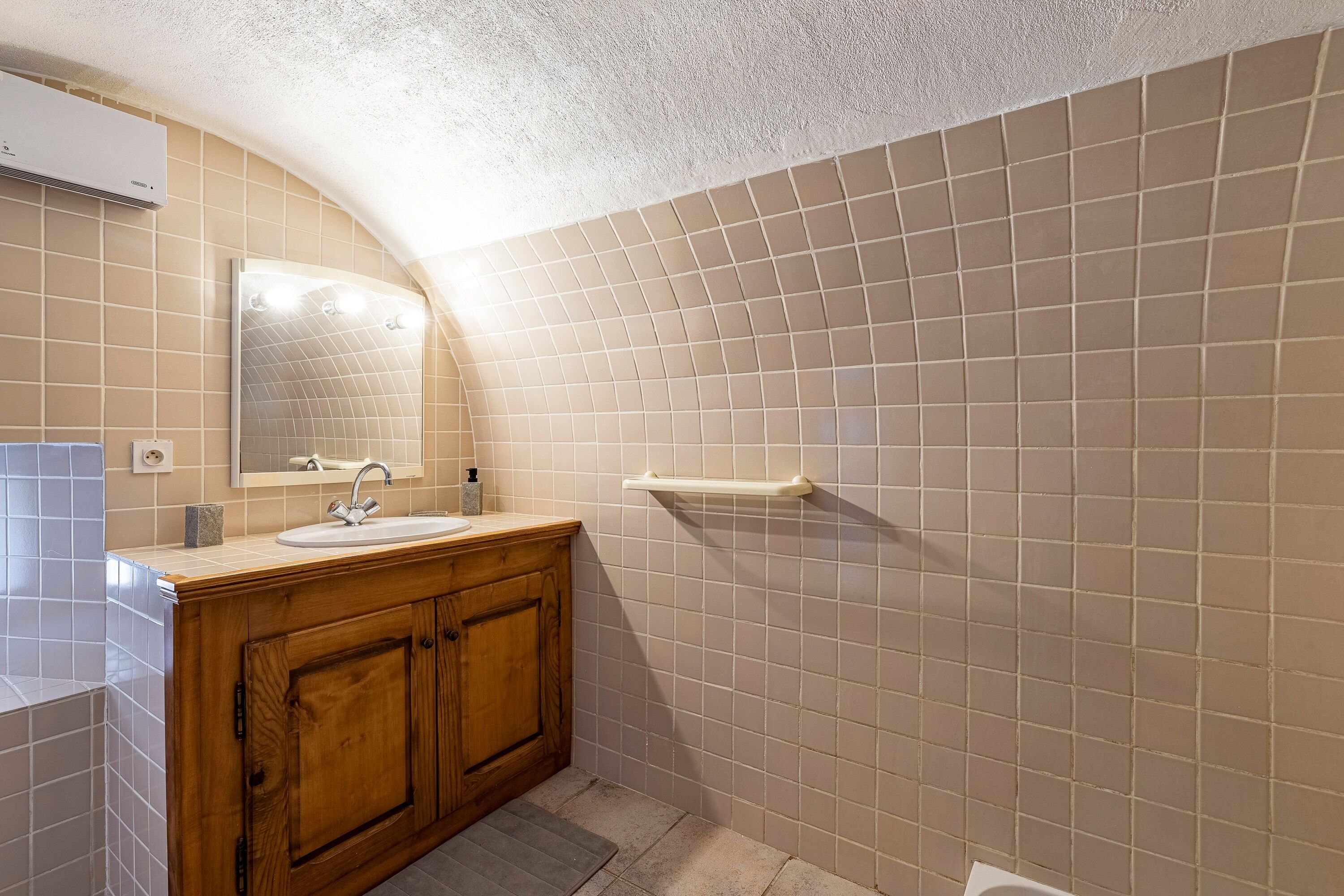 A bathroom with a wooden vanity, a mirror, a sink, and a tiled wall.