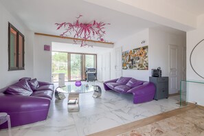 Ein modernes Wohnzimmer mit zwei violetten Ledersofas, einem Glastisch und einem großen, abstrakten Gemälde an der Wand.
