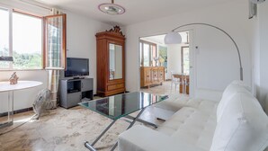 Ein modernes Wohnzimmer mit Glastisch, weißem Sofa, Holzschrank, Fernseher und Deckenventilator.