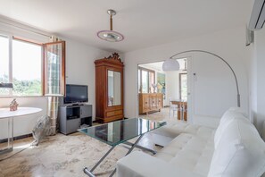 Ein modernes Wohnzimmer mit Glastisch, weißem Sofa, Holzschrank, Fernseher und Deckenventilator.