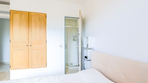 Ein Schlafzimmer mit einem Bett, einem Holzschrank, einem Badezimmer mit Dusche und einer weißen Wand.