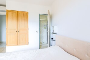 Ein Schlafzimmer mit einem Bett, einem Holzschrank, einem Badezimmer mit Dusche und einer weißen Wand.
