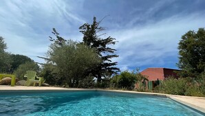 Ein klarer Pool mit Holzterrasse, umgeben von Bäumen und einem Gebäude im Hintergrund.