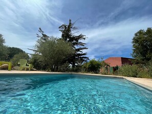 Ein klarer Pool mit Holzterrasse, umgeben von Bäumen und einem Gebäude im Hintergrund.