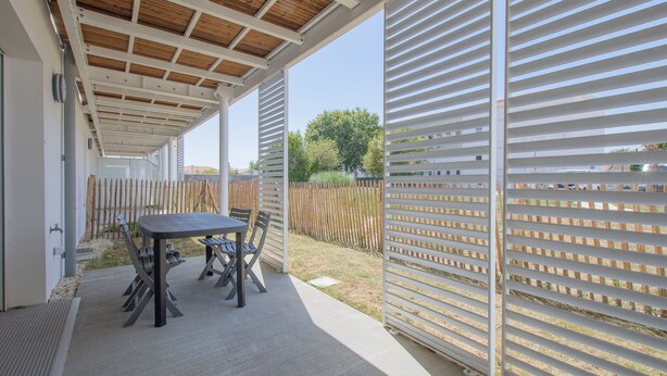 Eine Terrasse im Freien mit Tisch und Stühlen, einer Holzbeschichtung und Blick auf einen Zaun und Bäume.
