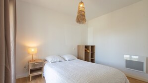 Ein Schlafzimmer mit Bett, Nachttischlampe, Holz-Nachttisch und einer gewobenen Leuchte.