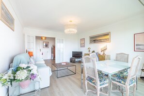 Ein Wohnzimmer mit Esstisch, Stühlen, einem Fernseher und einer Kandelaber.