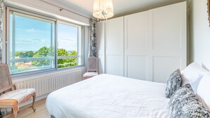 Ein Schlafzimmer mit einem großen Bett, einem Fenster mit Blick, einem Sessel und einem Kleiderschrank.