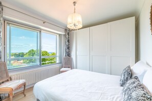 Ein Schlafzimmer mit einem großen Bett, einem Fenster mit Blick, einem Sessel und einem Kleiderschrank.