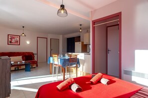 Ein Hotelzimmer mit einem roten Bett, einer Essecke mit Tisch und Stühlen, einem Sofa und einer durch eine offene Tür einsehbarer Küche.