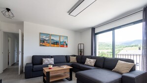 Ein modernes Wohnzimmer mit einem Ecksofa, einem Holztisch und einem großen Fenster mit Blick auf die Landschaft.